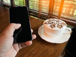 le café d'art latte et le jeune homme d'affaires tiennent un téléphone avec un écran d'espace vide pour la publicité, entrez un message ou un sujet de promotion au café. photo