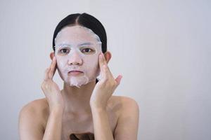 belle femme asiatique utilise un masque en feuille sur son visage. photo