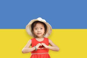 petite fille porte un chapeau montrant les mains en forme de coeur sur fond de couleur du drapeau ukrainien. arrêter la guerre pour la paix. aimer le concept de l'ukraine. photo