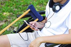 jeune ou personne handicapée assise sur un fauteuil roulant et ayant une béquille sur le côté, tout en portant des écouteurs pour écouter de la musique à partir de téléphones portables. concept de soins de santé et médical. photo