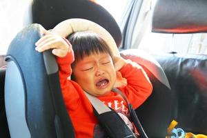 petit garçon qui pleure alors qu'il est attaché dans un siège d'auto de sécurité. enfant asiatique voyageant en voiture. photo