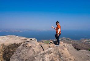 heureux homme asiatique debout avec un sourire heureux et le pouce vers le haut sur le point de vue supérieur sur le sommet de la montagne rocheuse avec vue sur le barrage du lac brumeux et ciel bleu photo