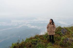 femme asiatique en manteau d'hiver debout sur le sommet de la montagne au point de vue 103 de pha tang avec vue sur la rivière et brume de mer et ciel de brouillard épais. lieu de voyage à chaing rai, thaïlande photo