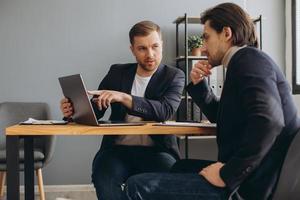 homme d'affaires sérieux discutant des détails du contrat ou trouvant une solution au problème avec un conseiller financier qualifié dans un bureau moderne. deux idées de projets de négociation de partenaires masculins réussis dans la salle de réunion. photo