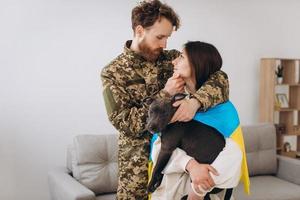 un couple ukrainien, un soldat en uniforme militaire et une fille enveloppée dans un drapeau ukrainien tiennent un chien dans leurs bras, heureux ensemble. photo