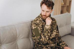 portrait d'un jeune soldat patriote ukrainien barbu émotionnel en uniforme militaire assis sur le canapé du bureau photo