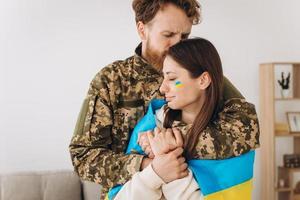 couple ukrainien, militaire en uniforme embrasse et enveloppe sa femme dans le drapeau ukrainien. la notion de patriotisme. photo