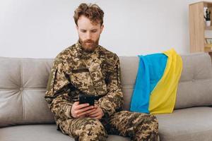 un soldat ukrainien en uniforme militaire est assis sur un canapé dans le bureau et parle au téléphone photo