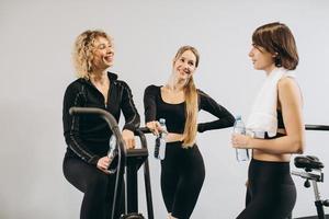 groupe de femmes dans la salle de sport se parlant de l'eau potable après s'être entraîné dans la salle de sport sur des vélos pneumatiques photo