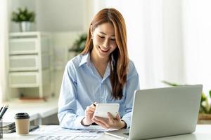 portrait d'une jeune femme asiatique travaillant sur un ordinateur portable et un rapport financier au bureau. photo