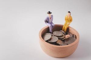 personnes miniatures. assis sur un bol en bois avec des pièces sur un fond blanc. concept d'économie d'argent. photo