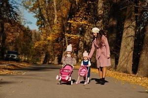 mère et deux petites filles avec poussette marchant sur le parc d'automne. photo