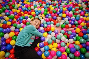 frère avec soeur jouant dans la piscine à balles colorées. garderie aire de jeux intérieure. piscine à balles pour les enfants. jardin d'enfants ou salle de jeux préscolaire. photo