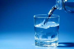 studio tourné de l'eau potable propre versée dans du verre et un fond bleu naturel. concept d'eau potable saine photo