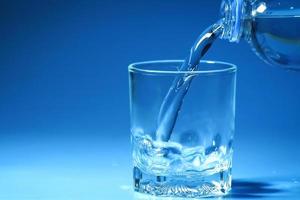 studio tourné de l'eau potable propre versée dans du verre et un fond bleu naturel. concept d'eau potable saine photo