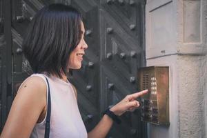 fille qui appuie sur un bouton de l'interphone de la maison à l'extérieur devant une immense porte antique. photo