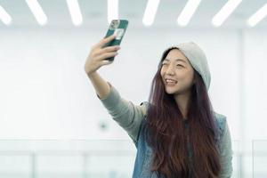 beau portrait jeune femme asiatique prenant un selfie avec un téléphone mobile intelligent, une fille photographie avec plaisir et sourit avec plaisir, concept de style de vie. photo