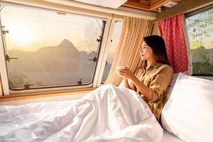 jeune femme voyageuse avec une tasse de café posée dans un camping-car et regardant un beau paysage pendant un voyage sur la route en vacances photo