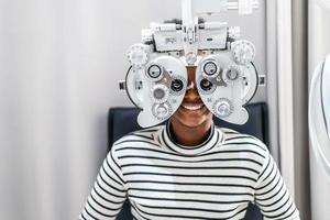 jeune femme souriante cheveux afro afro-américains faisant un test de la vue sur un réfracteur optique, vérifiant son œil avec une machine d'optométrie photo