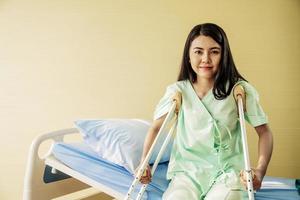 portrait d'une jeune patiente heureuse assise dans son lit avec des béquilles dans une chambre d'hôpital. concept de soins de santé et d'assurance médicale. photo