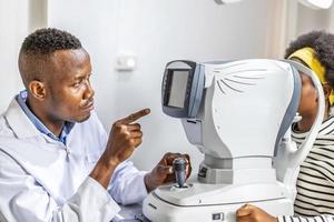 un médecin ophtalmologiste vérifie la vision oculaire d'une adolescente noire afro-américaine dans une clinique moderne. médecin et patient en clinique d'ophtalmologie. photo