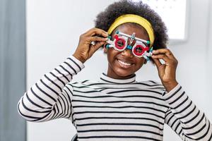 jeune femme souriante afro-américaine vérifiant la vision avec des lunettes de test oculaire lors d'un examen médical au bureau ophtalmologique, vérifiant la vision oculaire par le concept d'examen de santé opticien photo