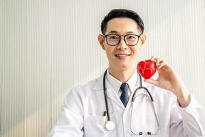 médecin avec stéthoscope montrant un coeur rouge au bureau de l'hôpital, soins de santé médicaux et concept de service de personnel médical. photo