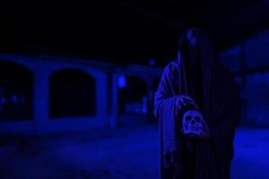 scène d'horreur d'un mystérieux homme noir effrayant tenant un crâne dans sa main dans un vieux couloir de bâtiment effrayant photo