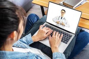 vue arrière d'une femme faisant un appel vidéo avec son médecin sur un ordinateur portable tout en restant à la maison, fille malade en consultation en ligne, assurance médicale, covid19 répandu. photo