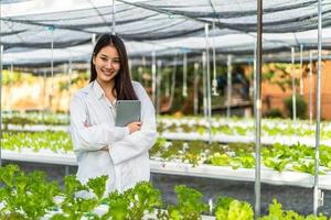 une chercheuse agricole asiatique debout avec les bras croisés s'occupe des légumes qui poussent à la ferme. l'agriculture est une agriculture durable pour l'alimentation future. photo