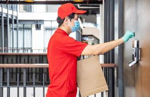 livraison directement à votre porte. jeune livreur asiatique portant un masque chirurgical et un gant pour la protection contre les virus tenant des sacs en papier de nourriture tout en frappant à la porte du bureau. photo