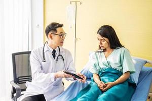 médecin de sexe masculin asiatique parlant à une patiente asiatique au lit, tout en expliquant les résultats de l'examen sur ordinateur au patient lors d'une consultation médicale, concept de médecine et de soins de santé, point de mise au point sélectif photo