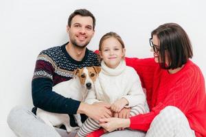 prise de vue en studio d'une famille heureuse de trois membres de la famille et d'un chien, embrasser et sourire joyeusement, avoir de bonnes relations, isolé sur fond blanc. beau petit enfant avec ses parents et son animal de compagnie préféré photo