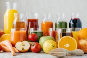 coup horizontal de fruits et légumes frais sur table blanche, bocaux en verre de jus et presse-agrumes orange. concept de boissons saines. boissons bio photo