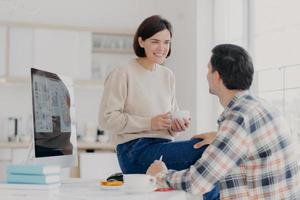 photo intérieure d'une jeune femme et d'un homme heureux discutent de quelque chose avec une boisson, utilisent un ordinateur moderne pour faire un rapport financier, posent dans une salle lumineuse spacieuse, collaborent ensemble pour faire une tâche commune