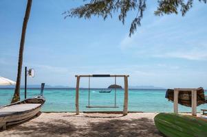 balançoire en bois sur la plage avec bateau en bois naviguant sur la mer tropicale photo