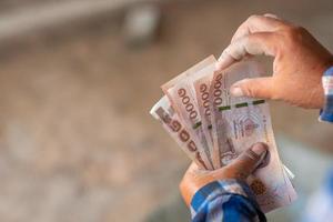 les mains d'un ouvrier du bâtiment tenant un billet d'une valeur de 5 000 bahts photo