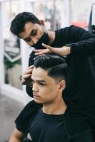 jeune homme au salon de coiffure. coiffeur coiffant les cheveux de son client dans un salon de coiffure pour hommes. soins personnels, beauté masculine. coiffeur. photo