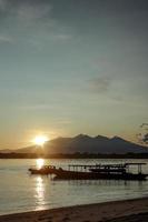 lever du soleil derrière la montagne avec des bateaux de pêche à longue queue bateaux traditionnels sur la mer à gili trawangan, bali, indonésie photo
