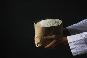 concept de fond de ramadan kareem. vue latérale d'une main musulmane tenant un sac d'aumône de riz isolé sur fond noir. zakat fitra photo