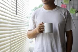 homme asiatique en chemise blanche tenant une tasse blanche pour maquette photo