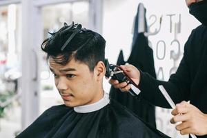 le coiffeur rase les cheveux du consommateur avec une tondeuse photo