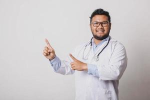 Cheerful male doctor avec geste de pointage latéral à l'espace de copie isolé sur fond blanc photo