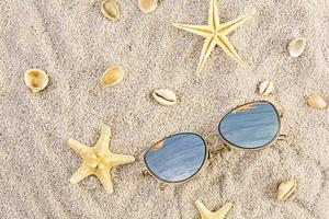 fond d'été. sable de mer avec coquillages, étoiles de mer et lunettes de soleil. notion de vacances d'été photo