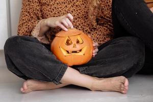 vue en coupe d'une femme adulte assise sur le sol à la maison avec une citrouille d'halloween sculptée. citrouille jack-o-lanterne, à l'intérieur. tour ou coffre. bonne journée d'halloween. mise au point sélective photo