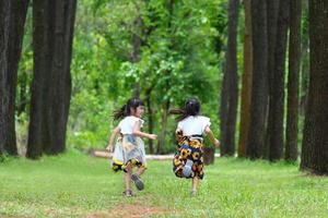 enfants heureux jouant sur l'herbe verte dans le jardin de printemps. deux petites soeurs courent sur un pré dans un parc d'été. photo
