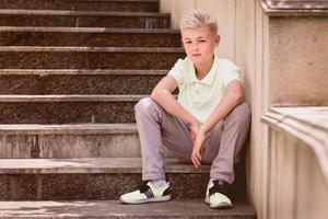 portrait de mignon beau blond onze vieux garçon assis sur les escaliers en plein air. grandir, enfance, concept de séparation photo
