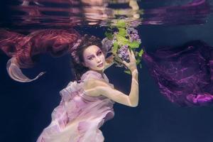 femme avec bouquet de lilas dans des vêtements colorés sur le fond sombre nageant sous l'eau photo