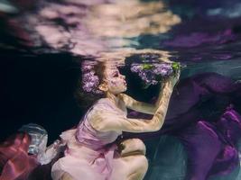 femme avec bouquet de lilas dans des vêtements colorés sur le fond sombre nageant sous l'eau photo