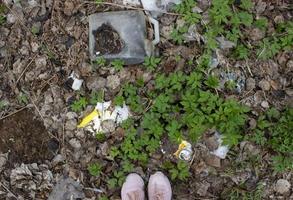 pieds debout sur le sol avec des feuilles sèches, de l'herbe verte et des ordures. notion de pollution de l'environnement. poubelle sous vos pieds photo